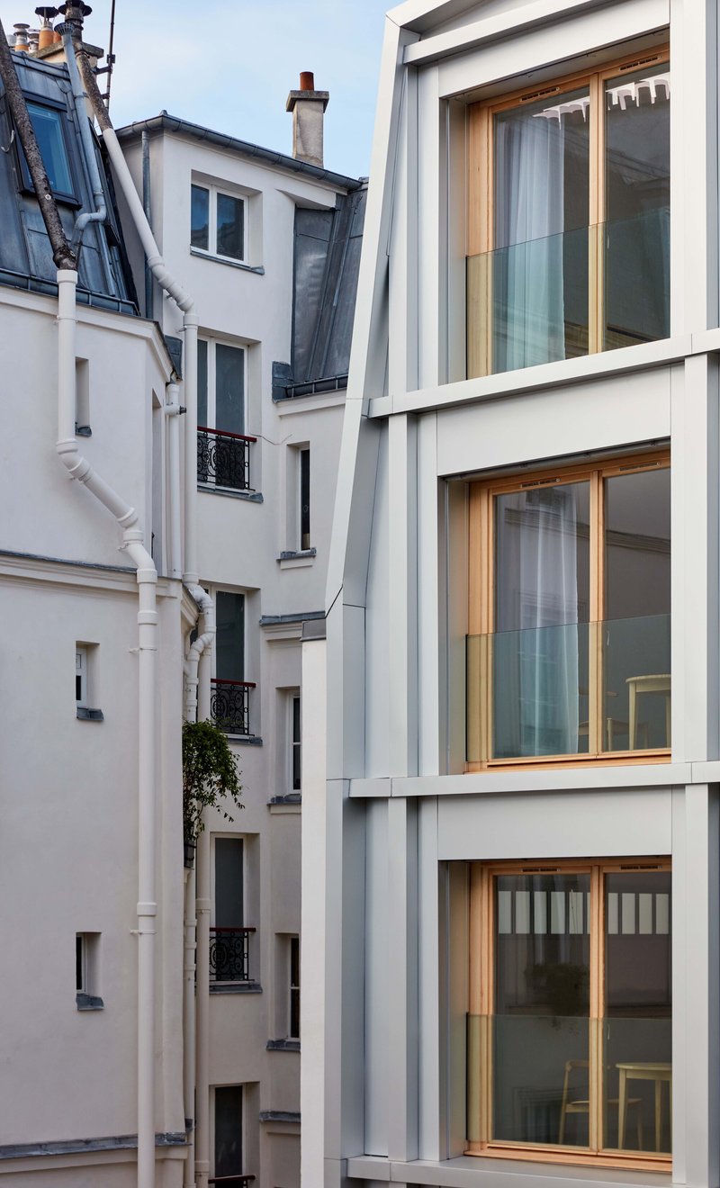 Rear elevation with recessed timber windows nestled between neighboring masonry buildings at twilight