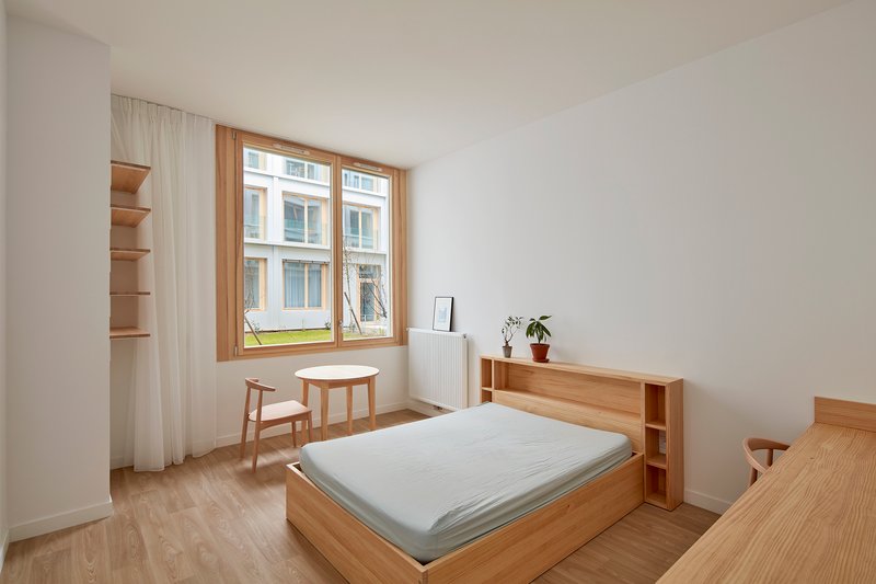 Bedroom with timber bed frame and open shelving beside a timber-framed window overlooking a courtyard