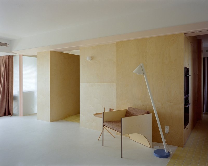 Interior with freestanding plywood volumes and a pale blue floor lamp beside a timber chair