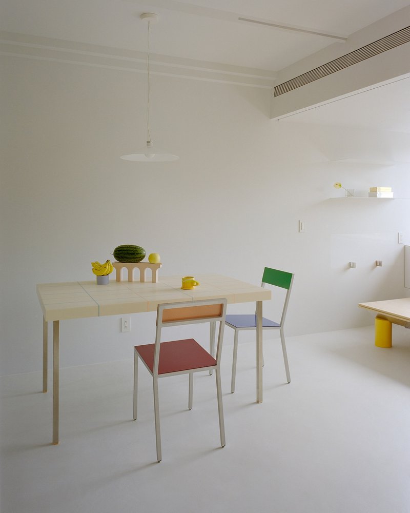 Dining area with pale wood table, colorful chairs and white pendant light overhead