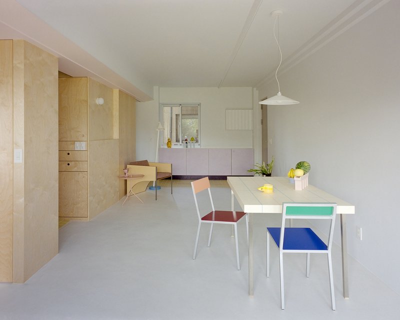 Open plan dining area with pale table and chairs with red blue and green seats