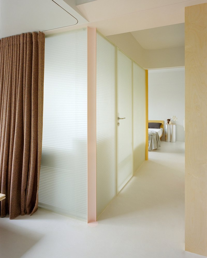 View through open doorway with yellow reveals leading to bedroom beyond translucent glass partition