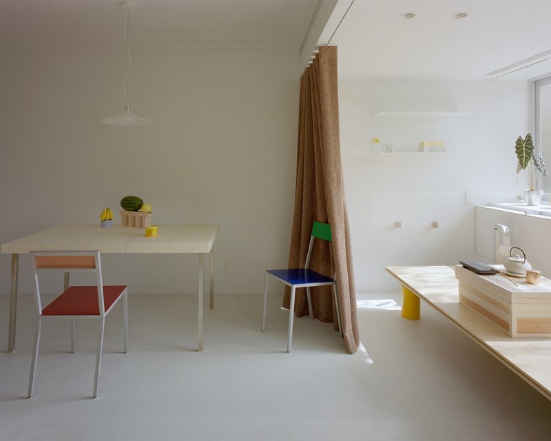 Dining area with stepped plywood counter and brown curtain dividing the white room