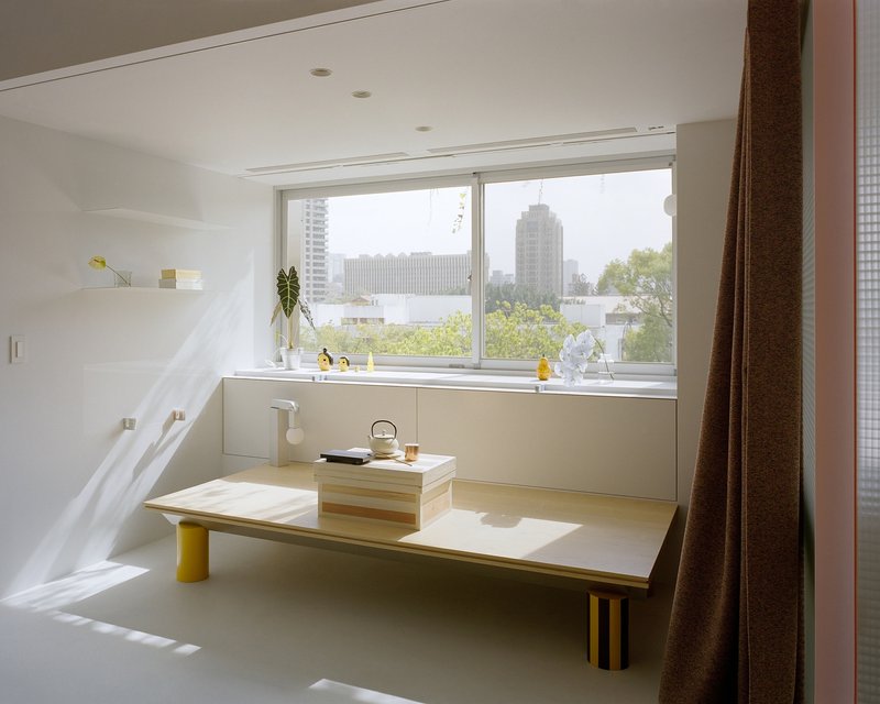 Low platform bench with yellow legs beneath a wide window overlooking the cityscape