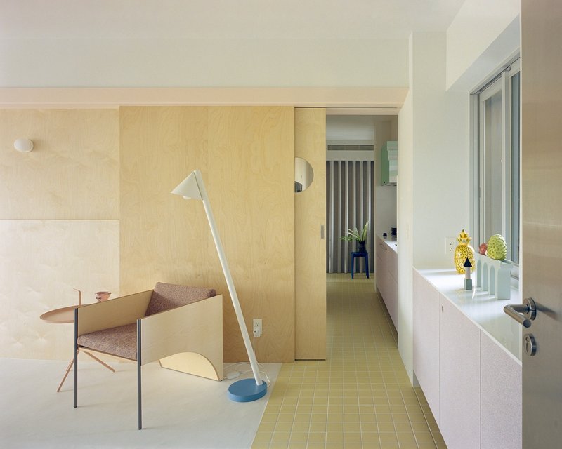 Plywood partition wall beside a corridor with yellow mosaic tiles leading to the bathroom