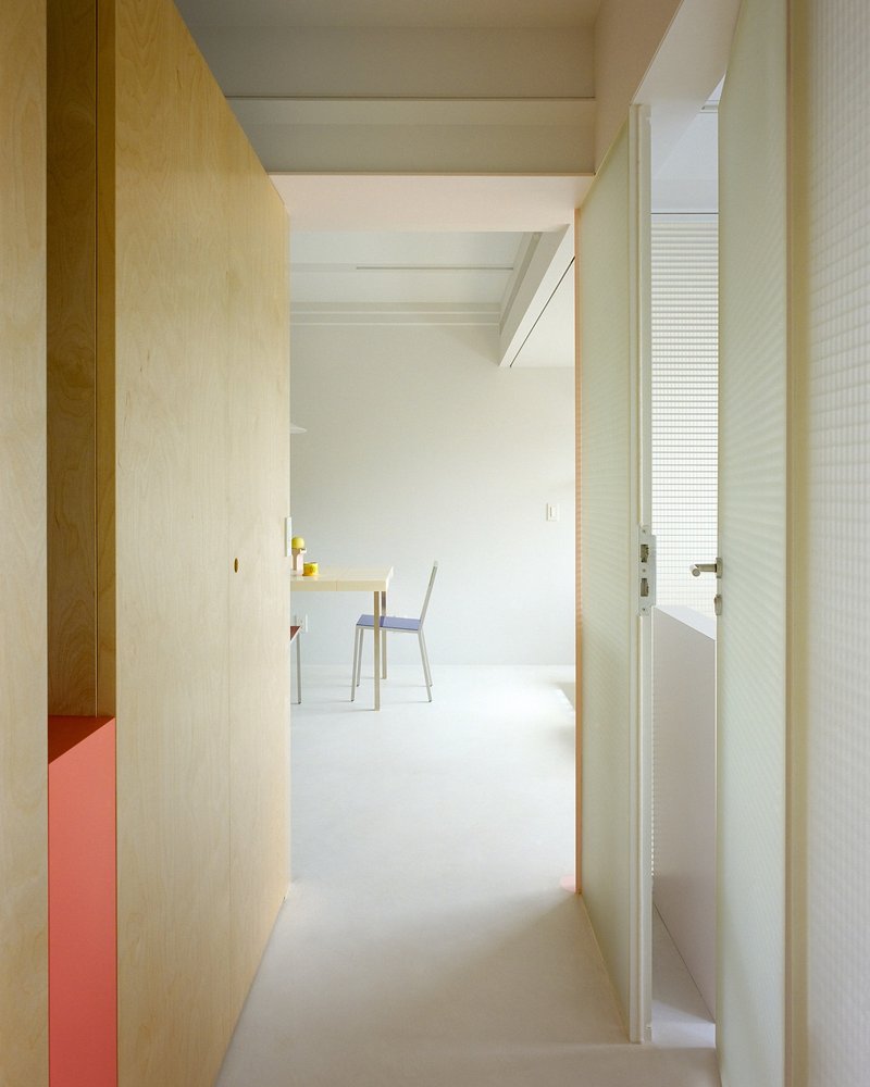 Narrow corridor with light plywood walls and white ceiling beams leading to a dining area