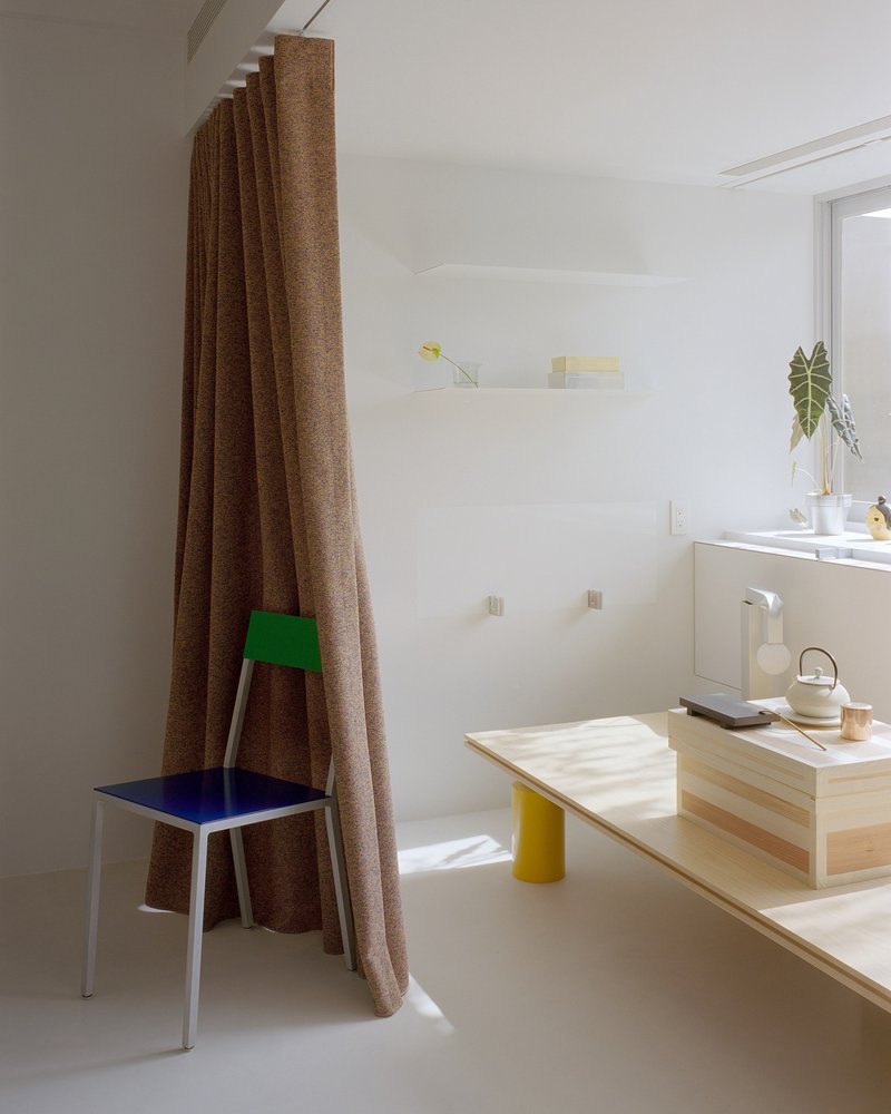 Interior corner with brown curtain, pale plywood bench with yellow legs and potted plant