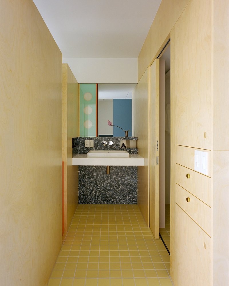 Bathroom vanity with terrazzo basin, yellow tile floor and plywood walls flanking a mirrored niche