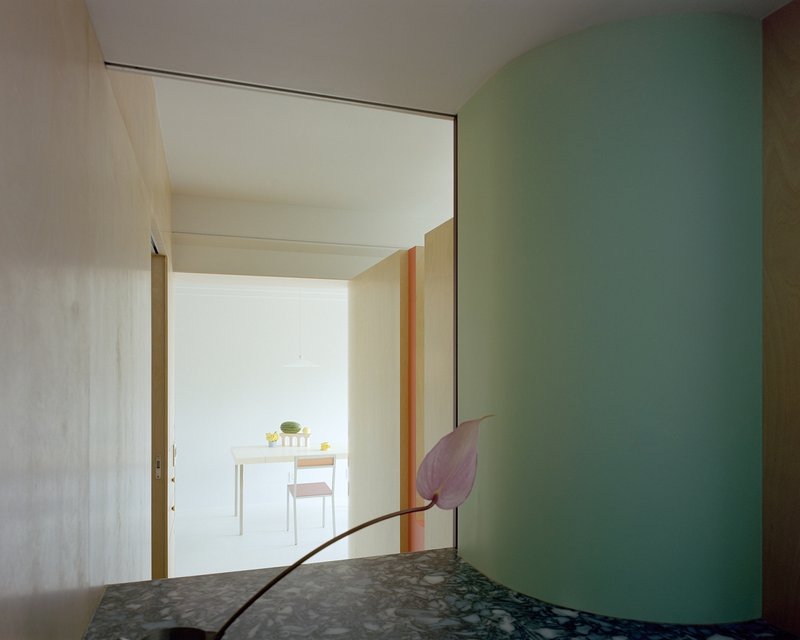 View through doorway past a terrazzo counter with single pink anthurium stem to dining area beyond