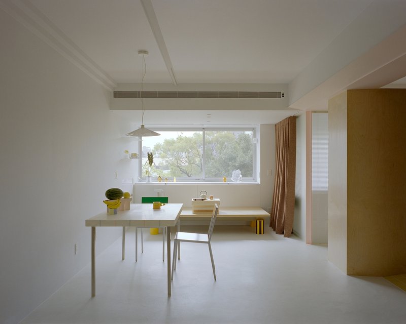 Dining area with pendant light, horizontal window framing green foliage and brown curtain at right