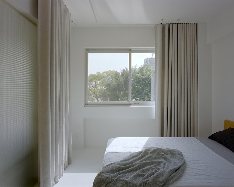 Bedroom with pleated curtain dividers and window overlooking distant residential towers