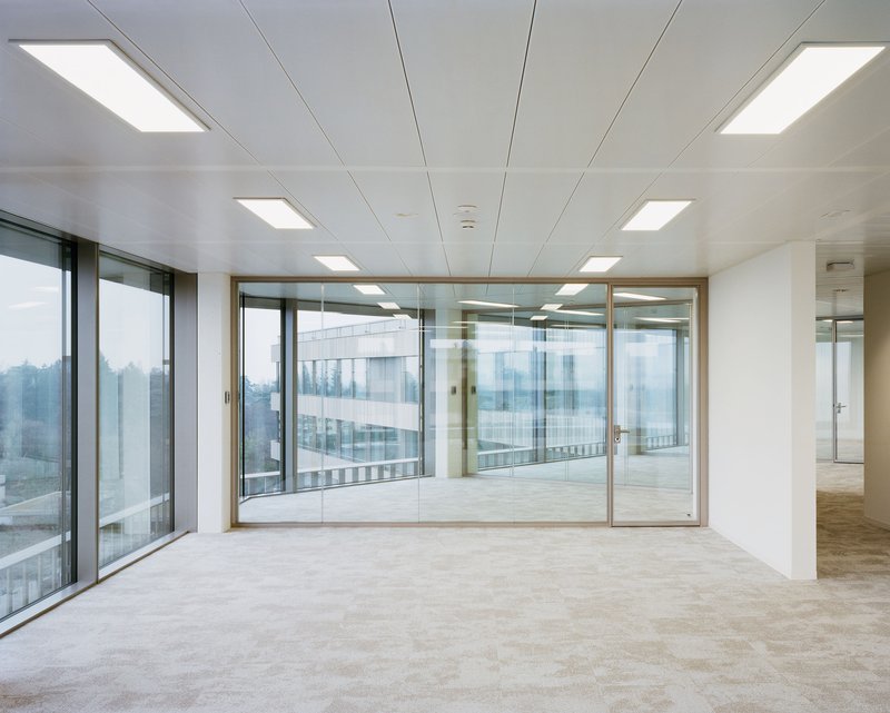 Open-plan office space with suspended ceiling panels and full-height glazed partitions