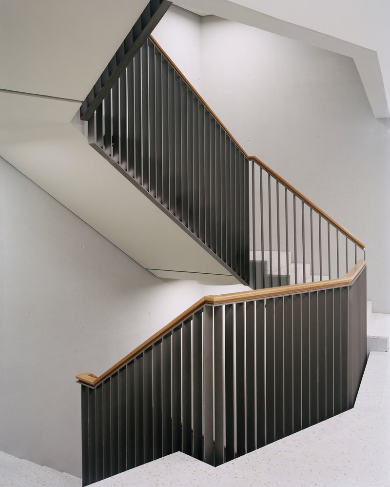 Switchback staircase with vertical black metal balustrades and timber handrails against white walls