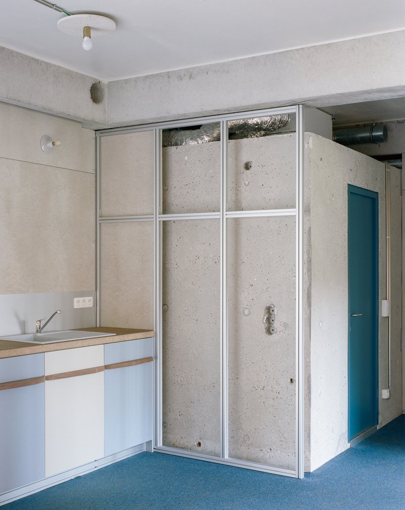Kitchen with white countertop and tall concrete panels framed by white metal mullions near blue door
