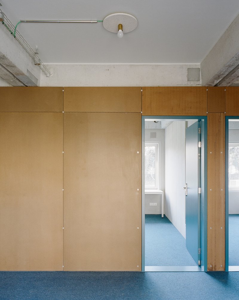 Plywood partition wall with blue rubber flooring and doorway revealing a corridor beyond