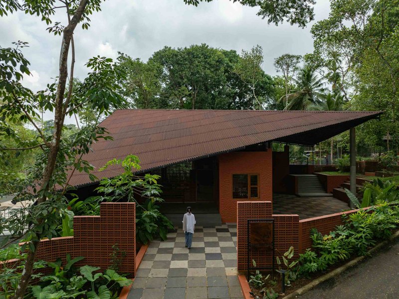Exterior view of sloped corrugated metal roof over terracotta walls within tropical vegetation under cloudy sky
