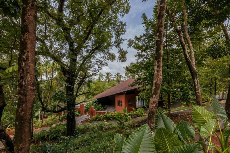 Red-roofed structure nestled among mature trees and tropical vegetation under a cloudy sky