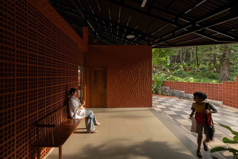 Interior corridor with textured terracotta walls and gridded screening as a woman sits and children play