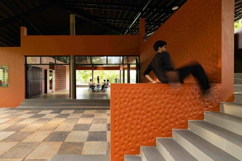 Terracotta-clad staircase with textured wall panels as a person descends toward an open pavilion beyond
