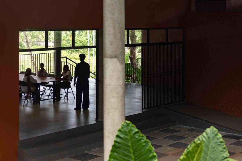 View through a wide doorway to the covered terrace where people gather at tables surrounded by forest