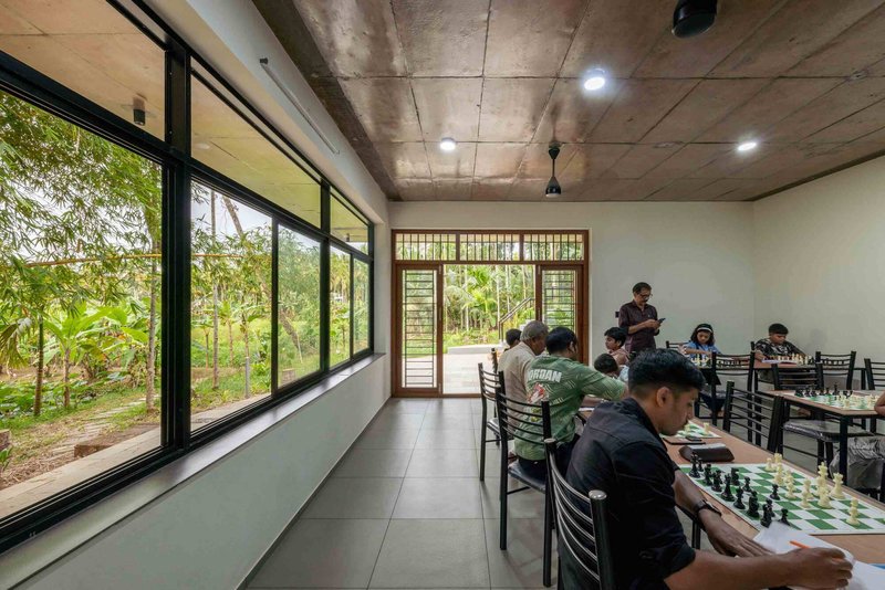 Long room with exposed concrete ceiling and continuous glazing opening to the wooded landscape beyond