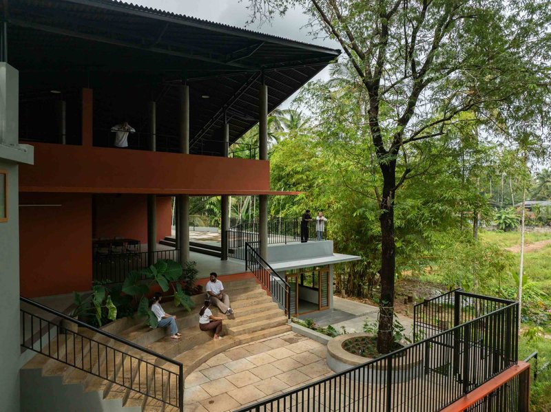 Multilevel courtyard with outdoor stairs and platforms where people sit beneath a broad overhanging roof