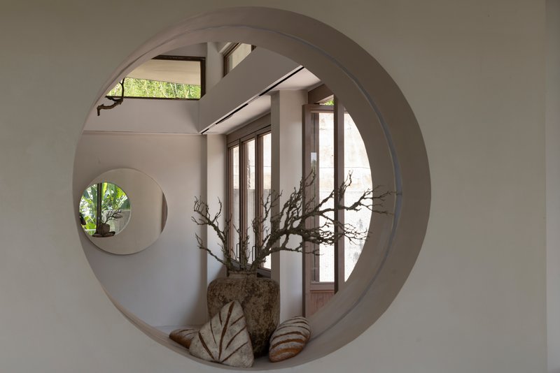 Interior view through circular wall opening revealing a second round aperture and natural light beyond