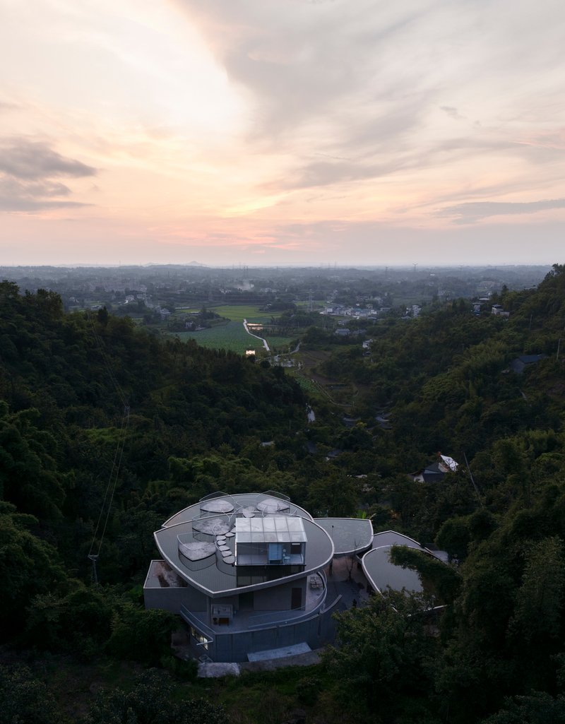 Aerial view of multi-lobed roof structure nestled in forested hillside at dusk
