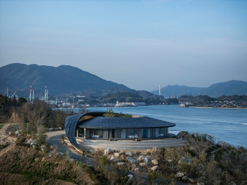 Side view of the glass-walled pavilion with its sweeping roof form overlooking the calm water