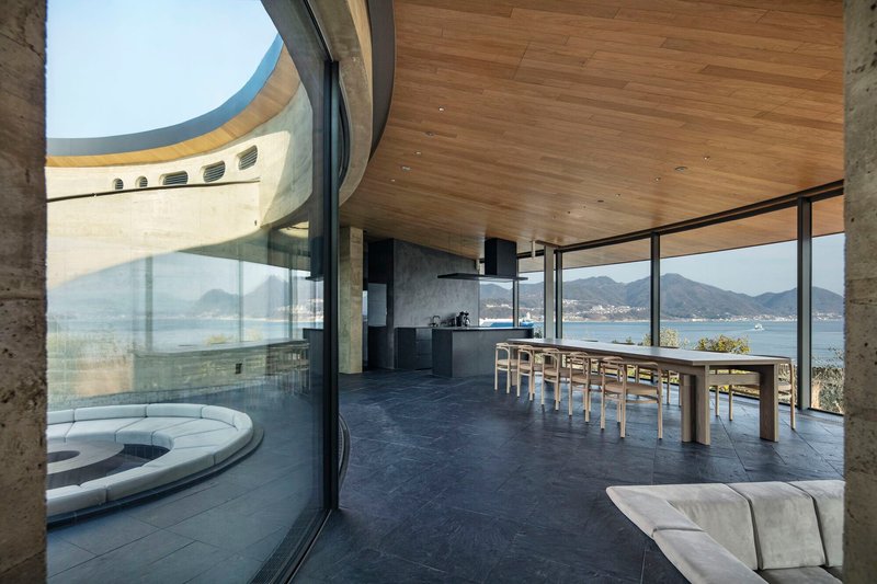 Interior dining area with timber ceiling, dark stone floor and glazed walls opening to the waterfront
