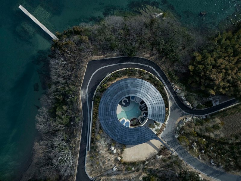 Aerial view of the circular roof with central oculus surrounded by planted terrace and lake water