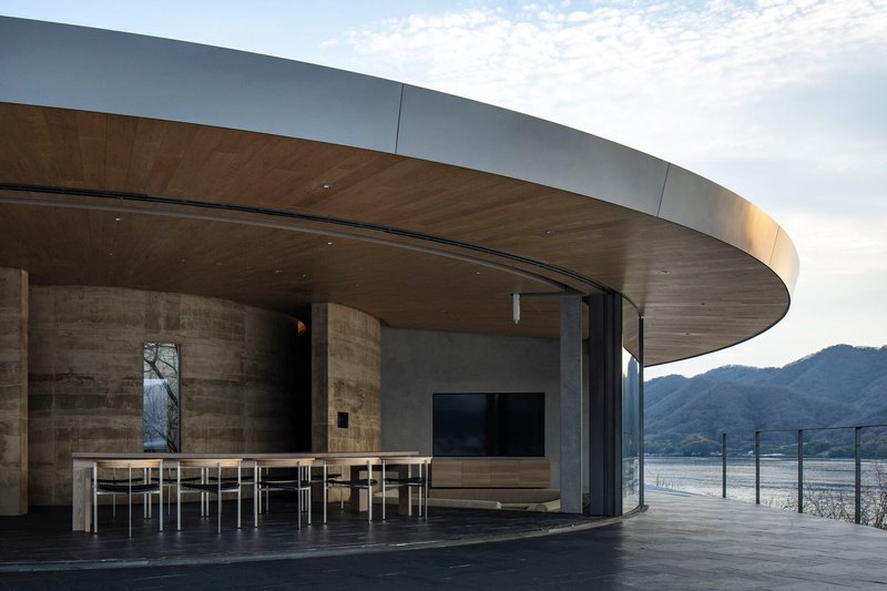 Covered terrace with overhanging disc roof, timber ceiling soffit and dining table facing the lake