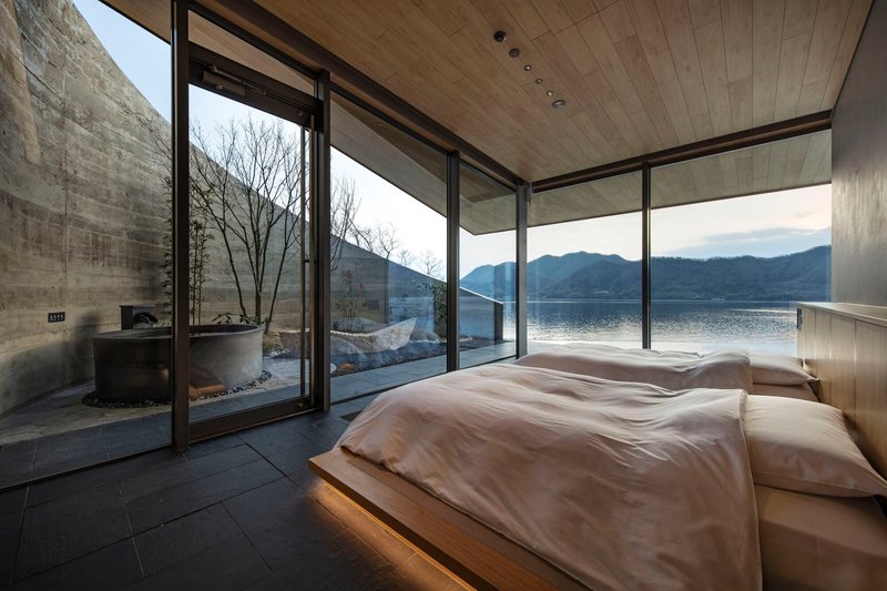 Floor-to-ceiling glazing opening the bedroom to a terrace with bare winter trees and lake view