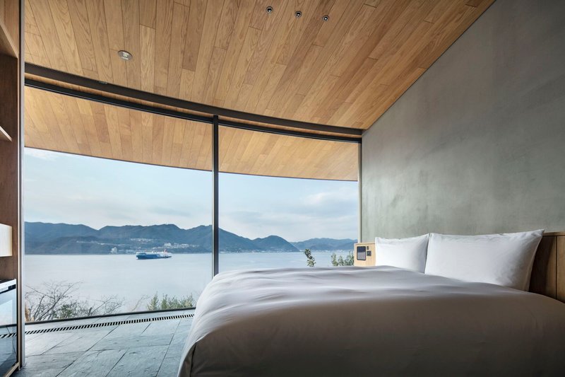 Bedroom with timber plank ceiling overlooking the lake and distant mountains under overcast skies