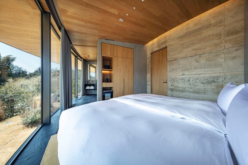 Bedroom with board-formed concrete walls and glazed corner opening to hillside vegetation