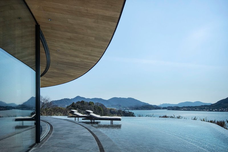 Infinity pool terrace with timber ceiling overhang overlooking a lake and distant mountain range at midday