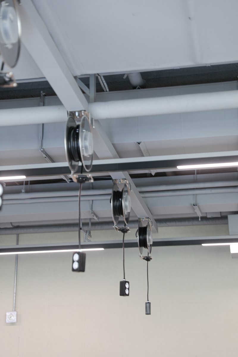Close-up of ceiling pulley system with steel cables and pendant weights beneath linear light fixtures