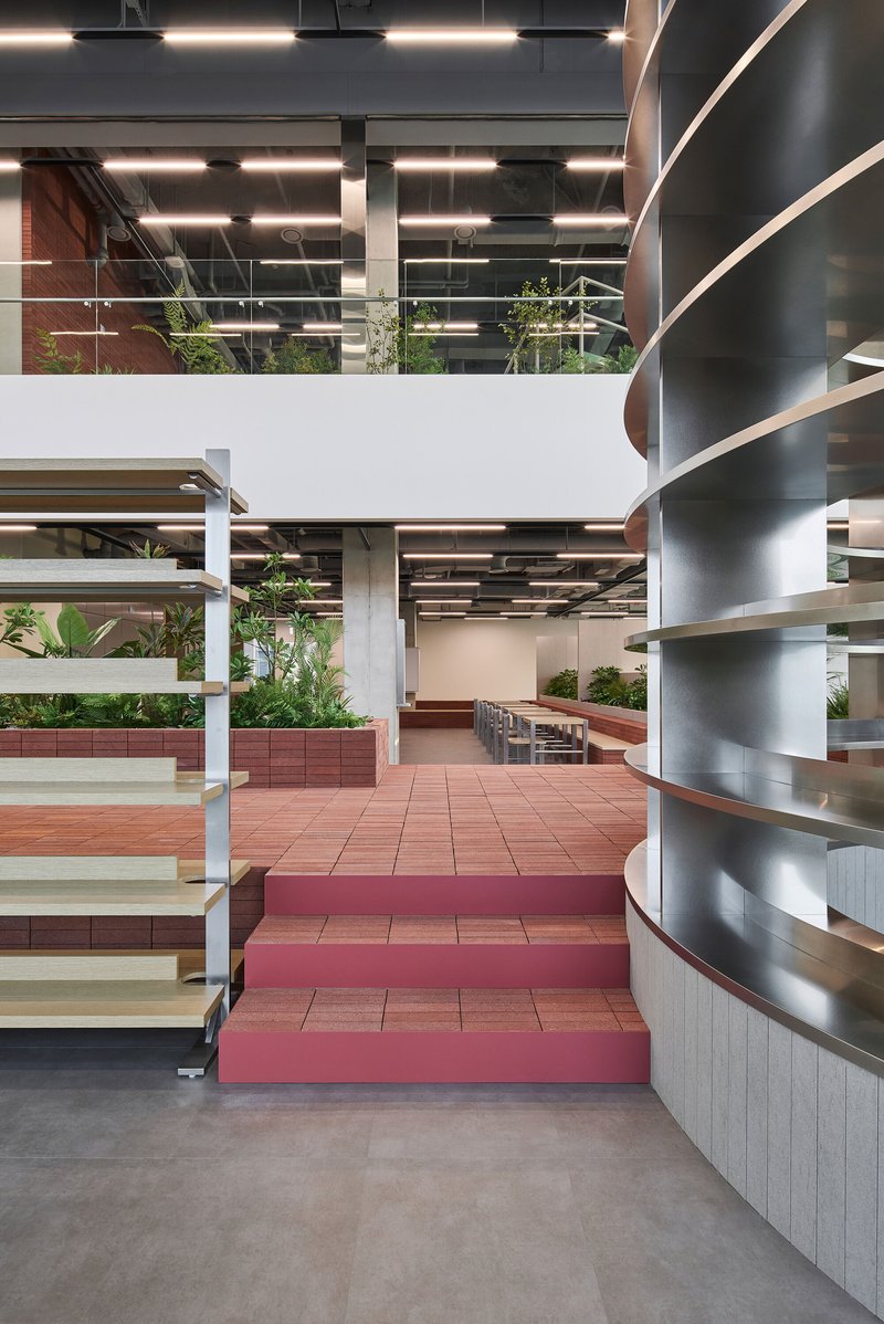 Tiered seating platforms in terracotta and burgundy tiles ascending toward white open-riser shelving units