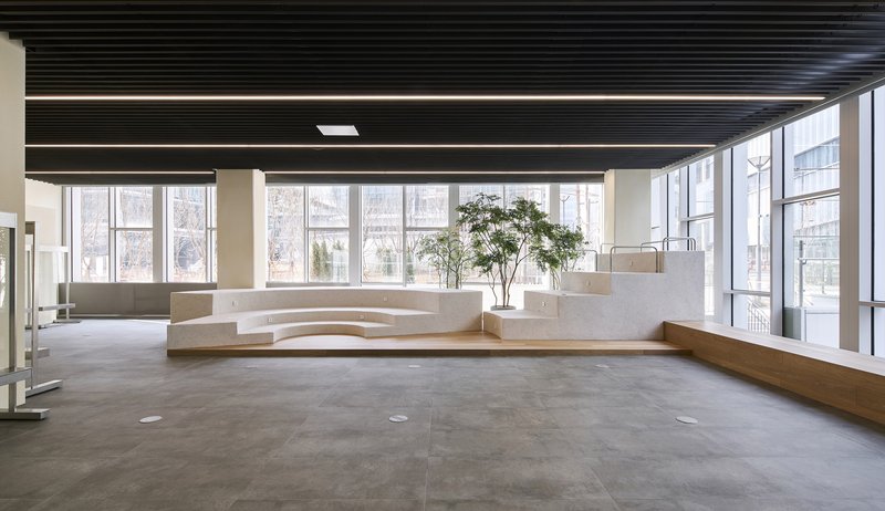 Curved white concrete seating plinth beside floor-to-ceiling windows under a black slatted ceiling