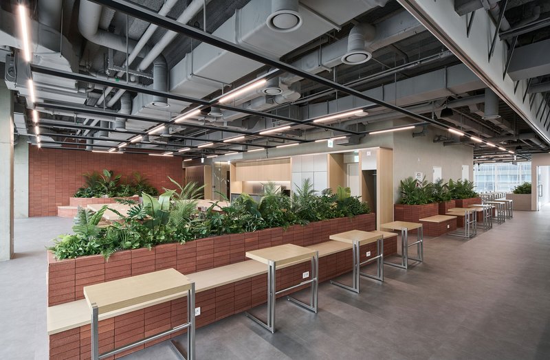 Rows of terracotta tile planters filled with greenery beneath a grid of exposed ductwork and linear lighting