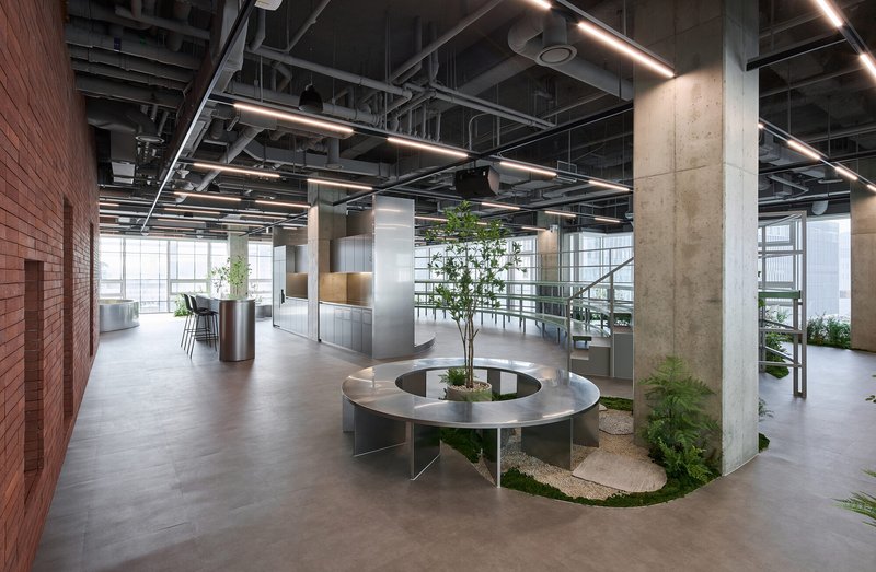 Open office floor with circular steel bench surrounding planted courtyard under exposed ceiling systems