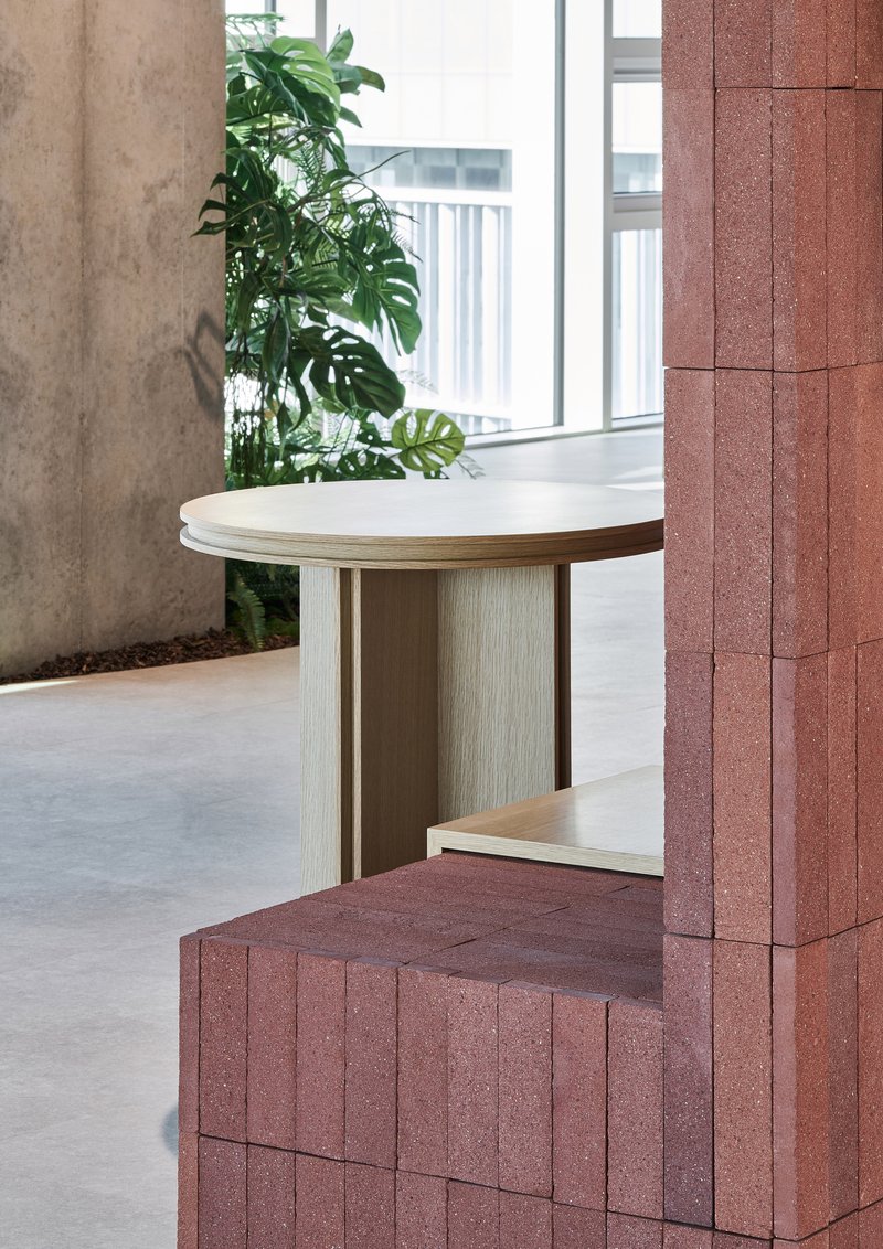 Red textured block column beside a light wood round table and monstera plant near a window