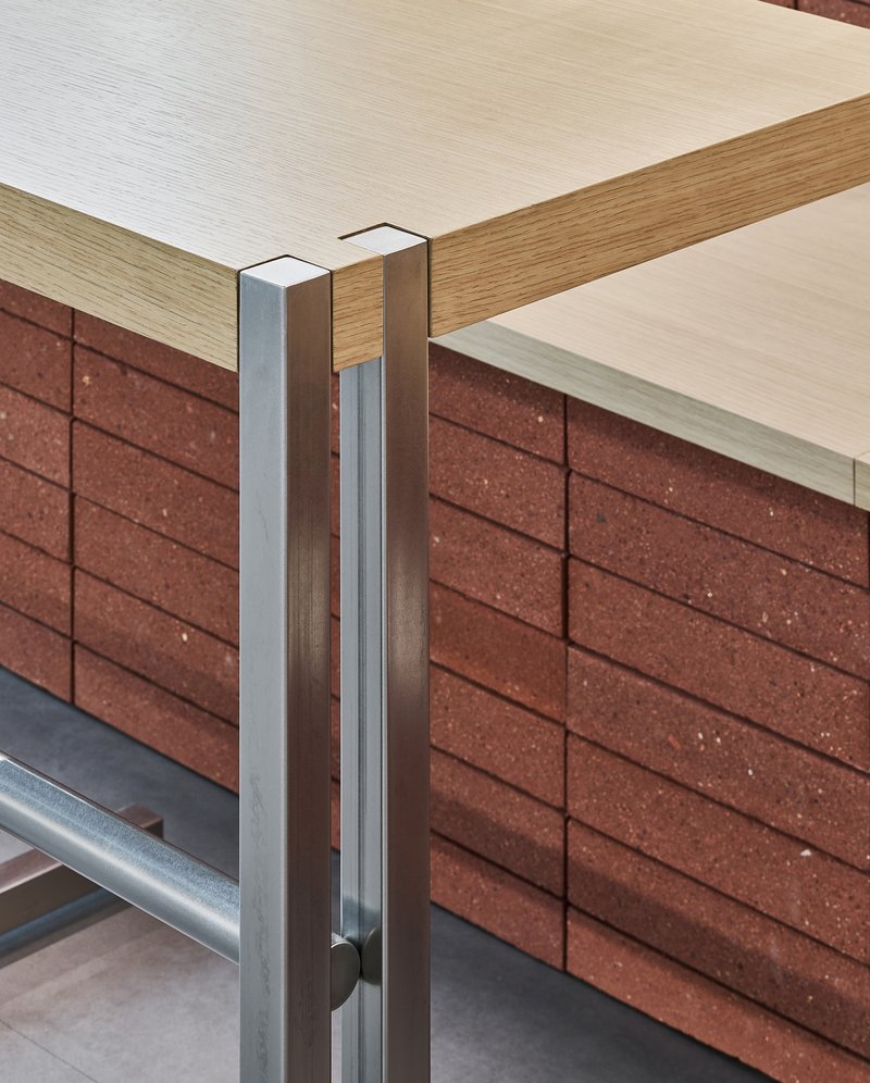 Junction detail of light wood table edge, metal bracket and red textured block base