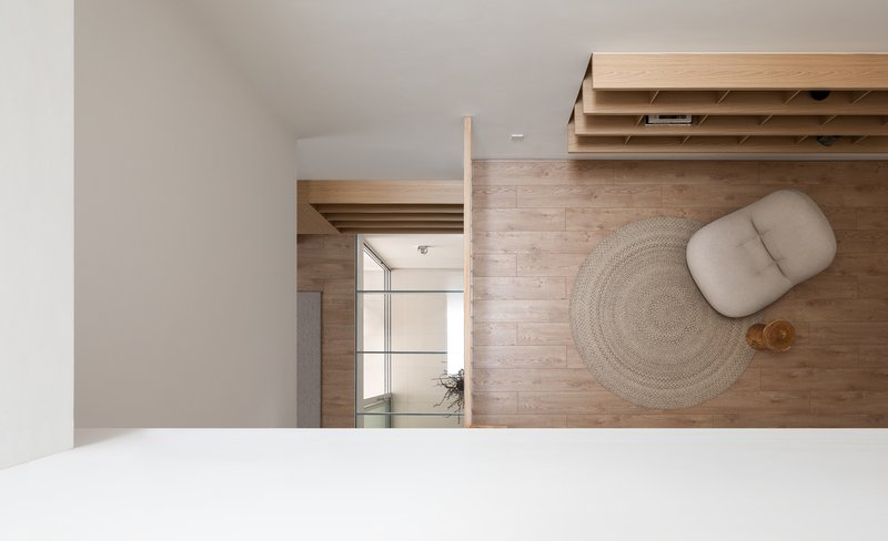 Overhead view of timber flooring with a woven rug and cushion beneath a timber storage unit