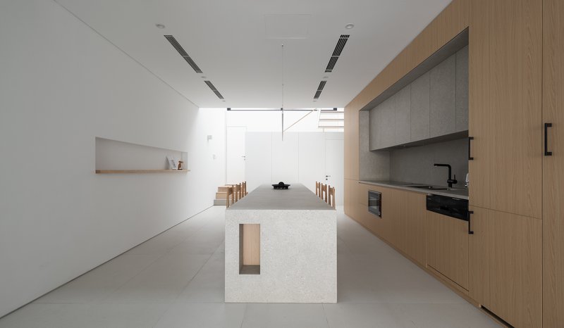 Open kitchen and dining area with a terrazzo island, timber cabinetry, and white walls under linear ceiling fixtures