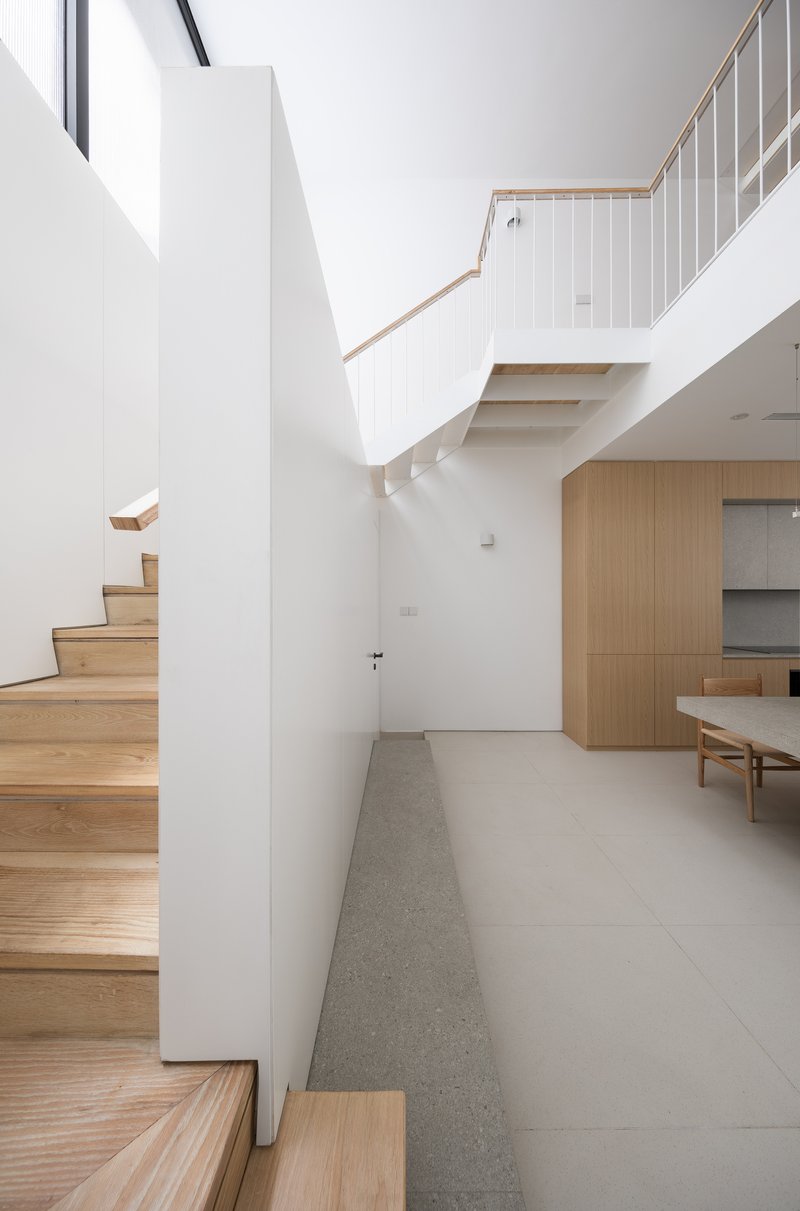 Timber staircase rising along a white wall beneath an upper landing with vertical railings