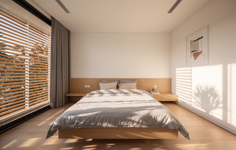 Bedroom with timber platform bed and horizontal timber louvres filtering morning sunlight