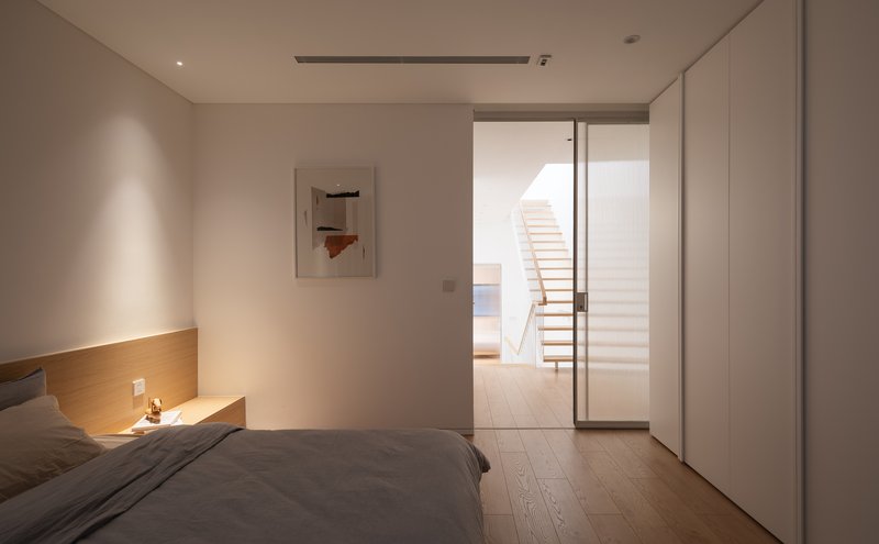 Bedroom with glass sliding door opening to hallway and floating staircase at dusk