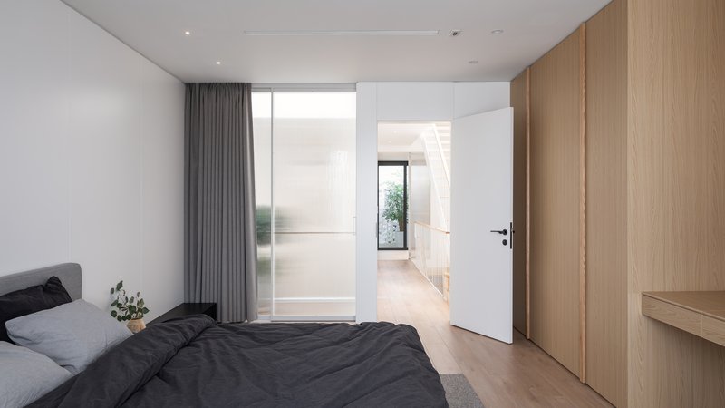 Bedroom with translucent glass partition and view through doorway to planted courtyard beyond