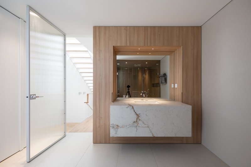 Bathroom vanity with marble countertop and timber surround beneath a staircase receiving daylight